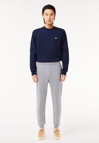 Hanorac bleumarin cu logo verde, pantaloni gri de tip joggers și adidași bej. Ansamblul are un croi lejer și o talie elastică.