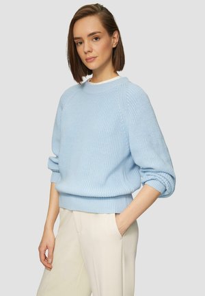 Hellblaue gestrickte Pullover mit runder Halslinie, fallenden Schultern sowie gerippten Bündchen und Saum; kombiniert mit cremefarbenen, weit geschnittenen Hosen.