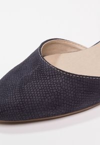 Chaussure plate noire à bout pointu avec une texture, doublure intérieure beige et coutures visibles le long du bord.