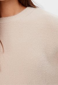 Pull rose clair, texture douce, avec un col rond. Gros plan sur l'aspect duveteux du tissu et les variations subtiles de couleur.