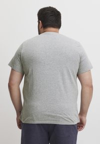 Tricou din bumbac gri, cu mâneci scurte și guler rotund, având o textură netedă. Croiala este relaxată și casual.