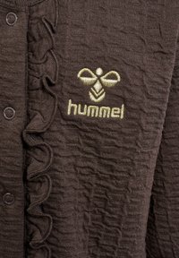 Bruntexturerad cardigan med volanger längs knapplist och en broderad logotyp i guld.