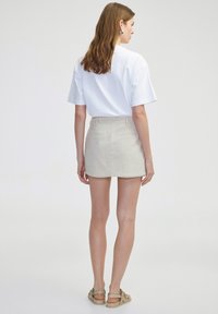 T-shirt blanc à manches courtes associé à une jupe mini en lin beige. L'ensemble présente un design simple sans motifs ni graphiques visibles.