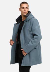 Kék bolyhos kabát kapucnival, fekete steppelt béléssel, oldalsó zsebekkel és hímzett logóval az ujján. Cipzáras záródás.