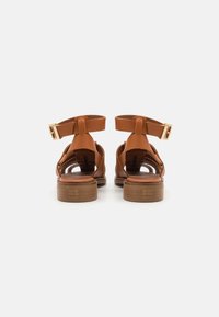 Braune Leder-Sandalen mit offenem Rücken und Knöchelriemen, mit einer goldenen Schnalle, flachem Holzabsatz und strukturiertem Innensohle.