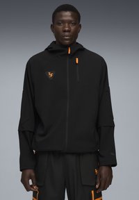 Sort lynlåset jakke med hætte, med orange detaljer og et logo på brystet. Mat stof med en strømlinet silhuet.