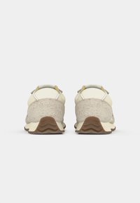 Sneaker mit einem beigen Obermaterial aus strukturiertem Stoff und glatten Akzenten, Gummisohle mit wellenförmigem Muster und verstärktem Absatz.