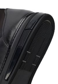 Zwarte leren schoenzool met een gestructureerd loopvlakpatroon en een gladde zwarte hielrand, schuin weergegeven voor een duidelijk beeld van het zoolontwerp.