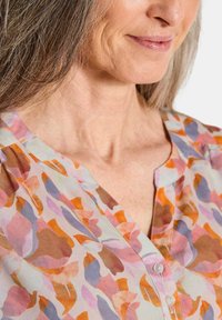 Knopfleiste-Bluse aus leichtem Stoff mit einem floralen Muster in Orange-, Pink- und Lavendeltönen, mit einem zarten Ausschnitt und Knöpfen.