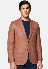 Brązowa marynarka w kratę o fakturowanej tkaninie, z zapięciem na dwa guziki i klapami wciętymi, zestawiona z granatową koszulą pod spodem.
