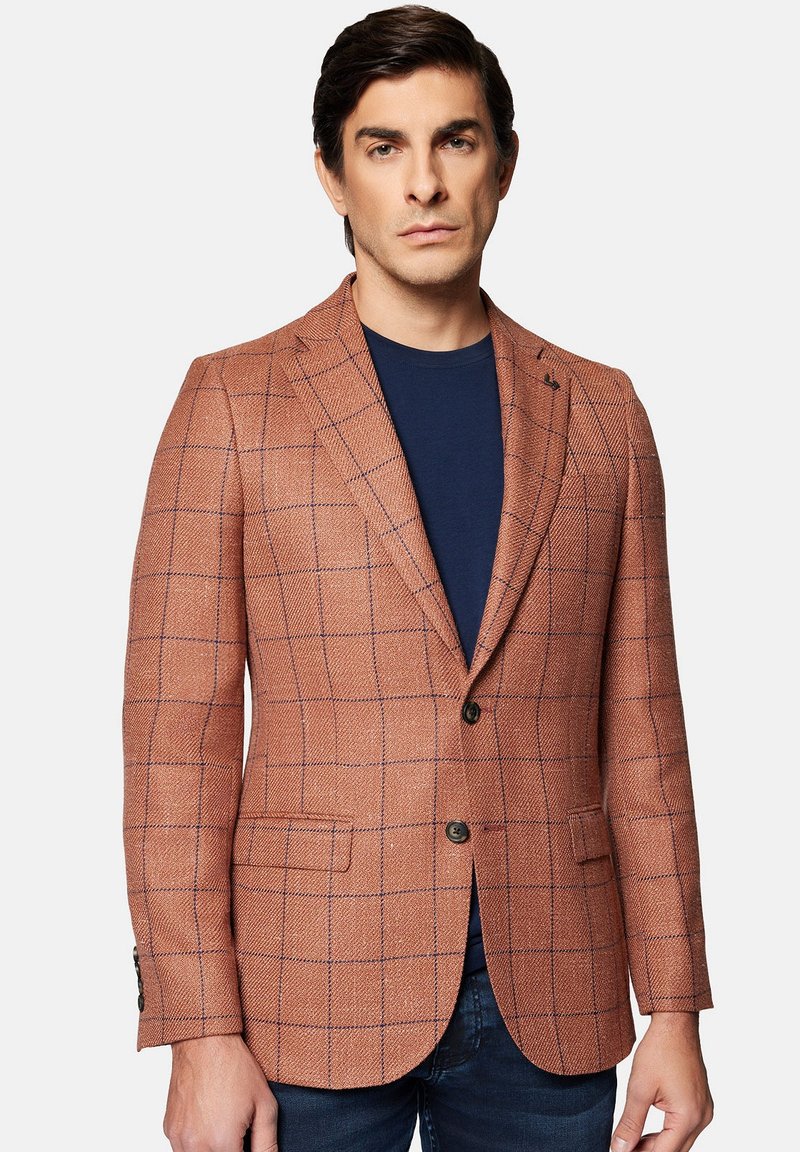 Brązowa marynarka w kratę o fakturowanej tkaninie, z zapięciem na dwa guziki i klapami wciętymi, zestawiona z granatową koszulą pod spodem.