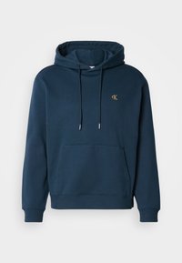 Felpa blu navy in misto cotone, presenta una tasca frontale, polsini a costine e un piccolo logo dorato sul petto. Texture morbida.