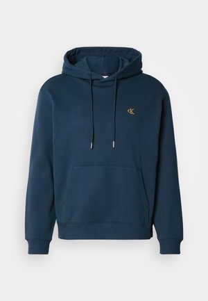 Felpa blu navy in misto cotone, presenta una tasca frontale, polsini a costine e un piccolo logo dorato sul petto. Texture morbida.