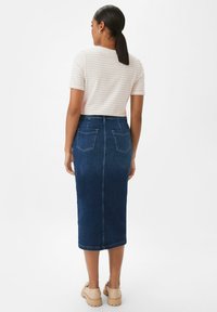 Denim skirt in dark blue with a fitted silhouette and back pockets. Paired with a light striped short-sleeve top.