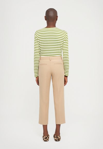 Vihreä- ja valkoraidallinen pitkähiha shirts, beige mukautetut housut ja pilkulliset korkokengät, nähtynä takaapäin neutraalilla taustalla.