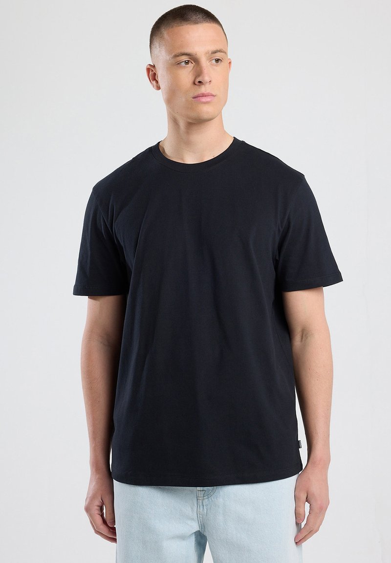 Camiseta negra de manga corta hecha de algodón. Diseño de cuello redondo, corte relajado y costuras mínimas. Se lleva con vaqueros azul claro.