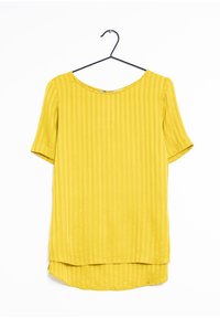 Blusa gialla a maniche corte con scollo rotondo, caratterizzata da una texture a righe verticali e un orlo posteriore più lungo. Appesa a un gancio nero.
