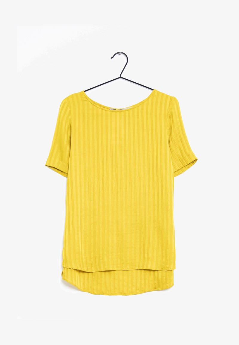 Blusa gialla a maniche corte con scollo rotondo, caratterizzata da una texture a righe verticali e un orlo posteriore più lungo. Appesa a un gancio nero.