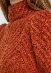 Pull tricoté orange rouille avec un col montant, présentant un motif texturé et des détails côtelés sur les épaules et les manches.