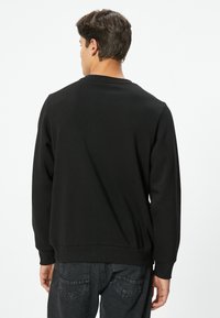 Sudadera negra con cuello redondo, puños y dobladillo acanalados. Presenta una textura suave y un ajuste casual, combinada con jeans oscuros.