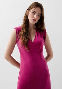 Fuksia ilmanhiha vestido, jossa on V-pääntie ja kerätty sivu. Valmistettu pehmeästä, sileästä materiaalista, joka myötäilee vartalon muotoja.