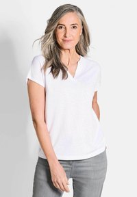 Top bianco a maniche corte con scollo a V e vestibilità comoda, realizzato in tessuto morbido. Abbinato a jeans grigi chiari, con maniche arrotolate e una sottile texture.
