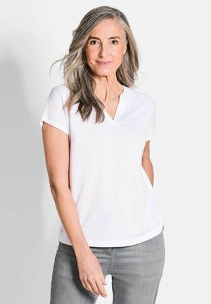 Witte T-shirt met korte mouwen en V-hals, met een losse pasvorm, gemaakt van zachte stof. Gepaard met lichtgrijze jeans met opgerolde mouwen en subtiele textuur.