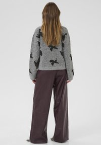 Maglione grigio con motivo di uccelli neri, abbinato a pantaloni in pelle larghi di colore bordeaux scuro. Texture morbida e vestibilità rilassata.