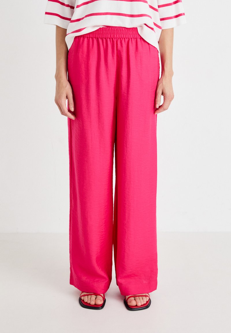 Wide-leg pink trousers made of lightweight fabric with an elastic waistband. Smooth texture with a flowing design, paired with black sandals.