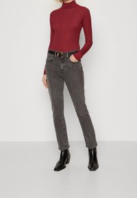 Top de cuello alto marrón y jeans gris de cintura alta, combinados con botas negras de tobillo. El conjunto incluye un cinturón negro con una hebilla circular dorada.