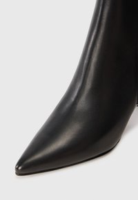 Bottine en cuir noir avec un bout pointu, texture lisse et un talon fin. Présente une silhouette élégante sans matériel ni accents visibles.