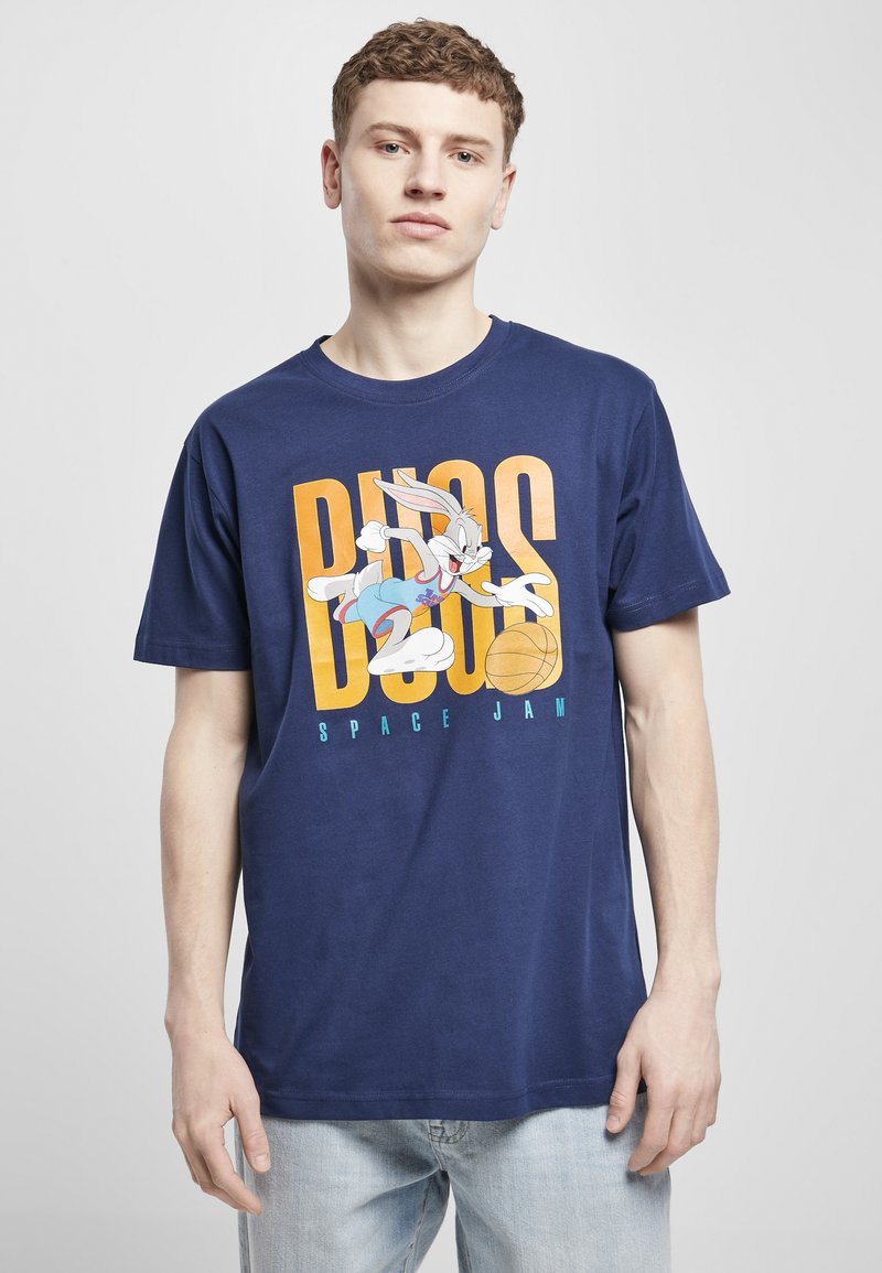 Tums zilā kokvilnas T-krekls ar grafiku, kurā attēlots Bugs Bunnijs un basketbola bumba, ar oranžiem un ziliem burtiem, kuri lasa "Bugs Space Jam."