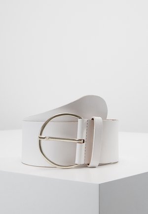 Witte leren riem met een grote ronde zilveren gesp, opgerold weergegeven op een wit oppervlak met hoeken tegen een effen achtergrond.