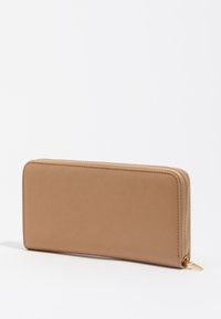 Billetera con cierre tipo zip en color beige, fabricada en material sintético suave; cuenta con un zipper dorado, forma rectangular y un diseño minimalista sin patrones.