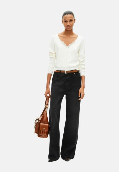 Hvid V-udskæring cardigan med blonderkant, parret med sorte brede bukser og en brun læderhåndtaske. Flade sko fuldender outfittet.