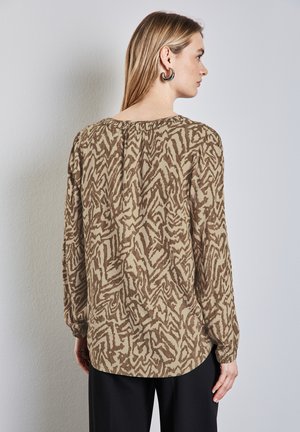 Blusa a maniche lunghe marrone con motivo, colletto rotondo, dettaglio arricciato sul retro e vestibilità comoda, abbinata a pantaloni neri.