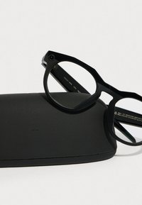 Schwarze rechteckige Brille mit einem dicken Rahmen und klaren Gläsern, auf einem mattschwarzen Hardcase positioniert.