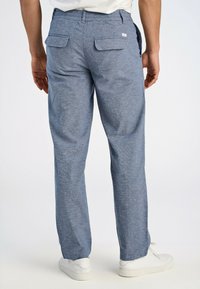 Jasnoniebieskie spodnie z mieszanki bawełny o teksturowanym wykończeniu, z elastycznym pasem, dwoma tylnymi kieszeniami i białymi sneakersami.