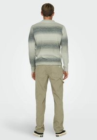 Pull all'uncinetto grigio ombre con colletto e polsini a coste, abbinato a pantaloni in velluto a coste beige chiaro con tasche posteriori e cuciture laterali.