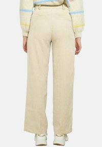 Pantalons larges en velours côtelé beige avec une surface texturée, taille haute et poches arrière, associés à des baskets blanches.