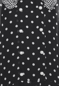 Robe noire à pois blancs, ornée d'un col volanté en vichy noir et blanc et de boutons en perles.