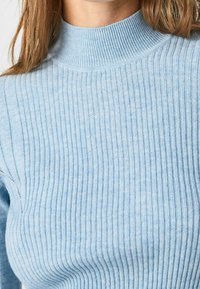 Pull en maille côtelée bleu clair avec un col montant douillet et une texture douce, mettant en valeur des lignes verticales et une silhouette ajustée.