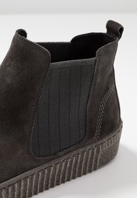 Bottine en daim noir avec un panneau latéral élastique texturé et une semelle côtelée. Comprend une languette à tirer pour un enfilage facile.