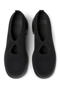 Chaussures noires sans lacets avec une texture tricotée, des découpes ovales et un talon épais. La semelle intérieure est marquée du nom de la marque "Camper".