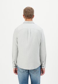 Camisa gris de manga larga con cuello abotonado, pliegue en la parte trasera y puños abotonados, combinada con jeans de mezclilla azules. Textura suave.