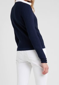 Sweater de punto en color marina con mangas largas y cuello redondo, combinado con pantalones blancos ajustados. Tejido texturizado con un acabado suave en el dobladillo.