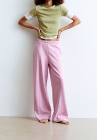 Světl zelený přiléhavý top s bílými akcenty, kombinovaný s volnými růžovými tepláky s elastickým páskem a bočními švy. Naboso.