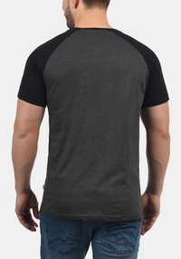 T-shirt à manches courtes gris et noir avec un design raglan, présentant une texture lisse. Porté avec un jean en denim bleu.