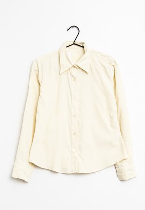 Lichtgele blouse met lange mouwen, een puntige kraag, knopen aan de voorkant en een zachte textuur, hangend aan een zwarte haak tegen een witte achtergrond.