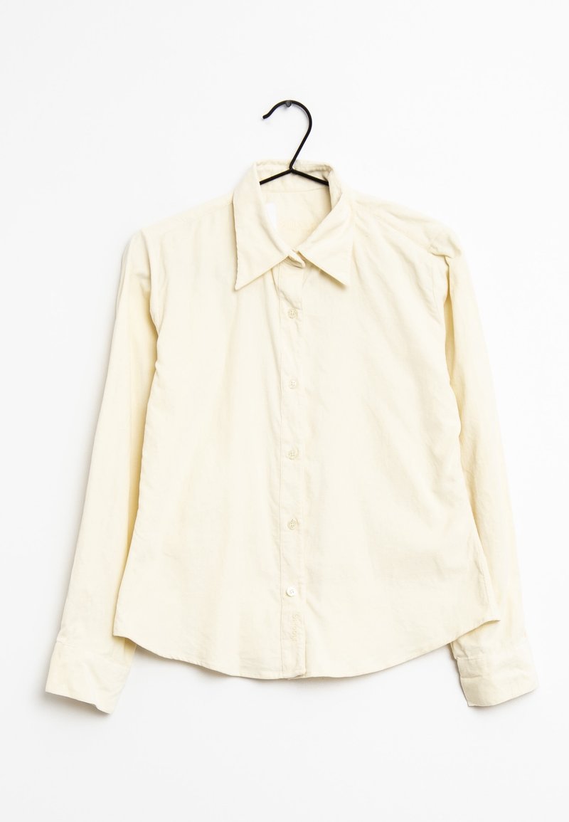 Hellgelbes Langarmhemd mit spitzem Kragen, vorderen Knöpfen und weicher Textur, hängt an einem schwarzen Haken vor einem weißen Hintergrund.